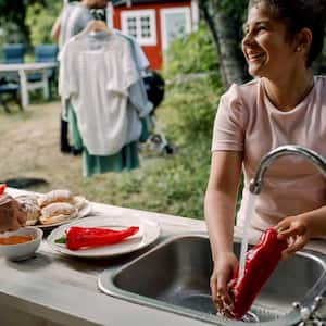 A young girl rinsing vegetables in an outdoor sink