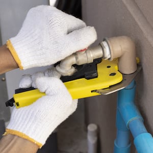 gloved hands holding pipe cutter against pipe