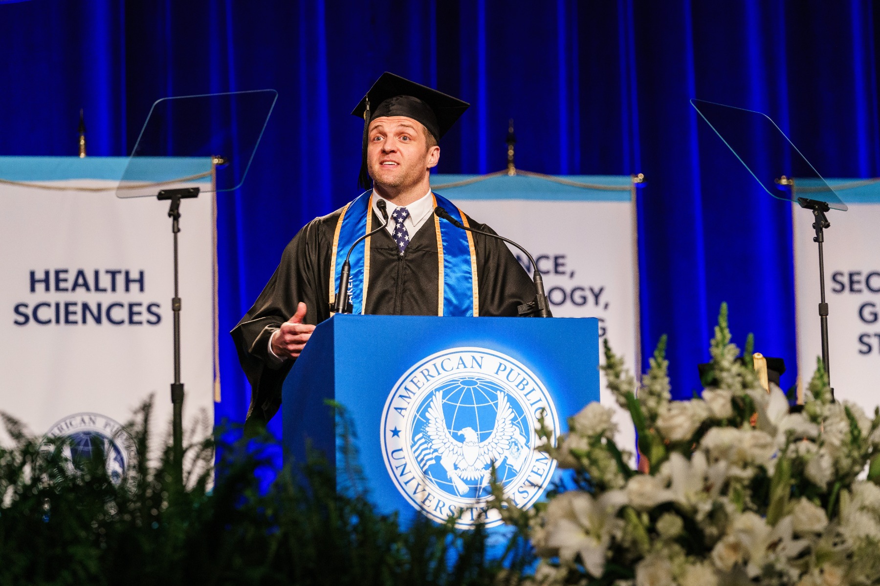 Man in graduation cap and gown giving speech during ceremony