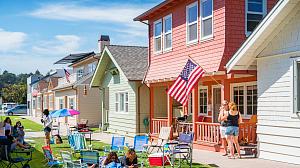 People sitting in the grass outside a colorful row of houses.