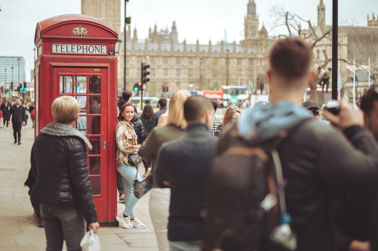 A woman is posing for a photo by leaning against a red phone booth.