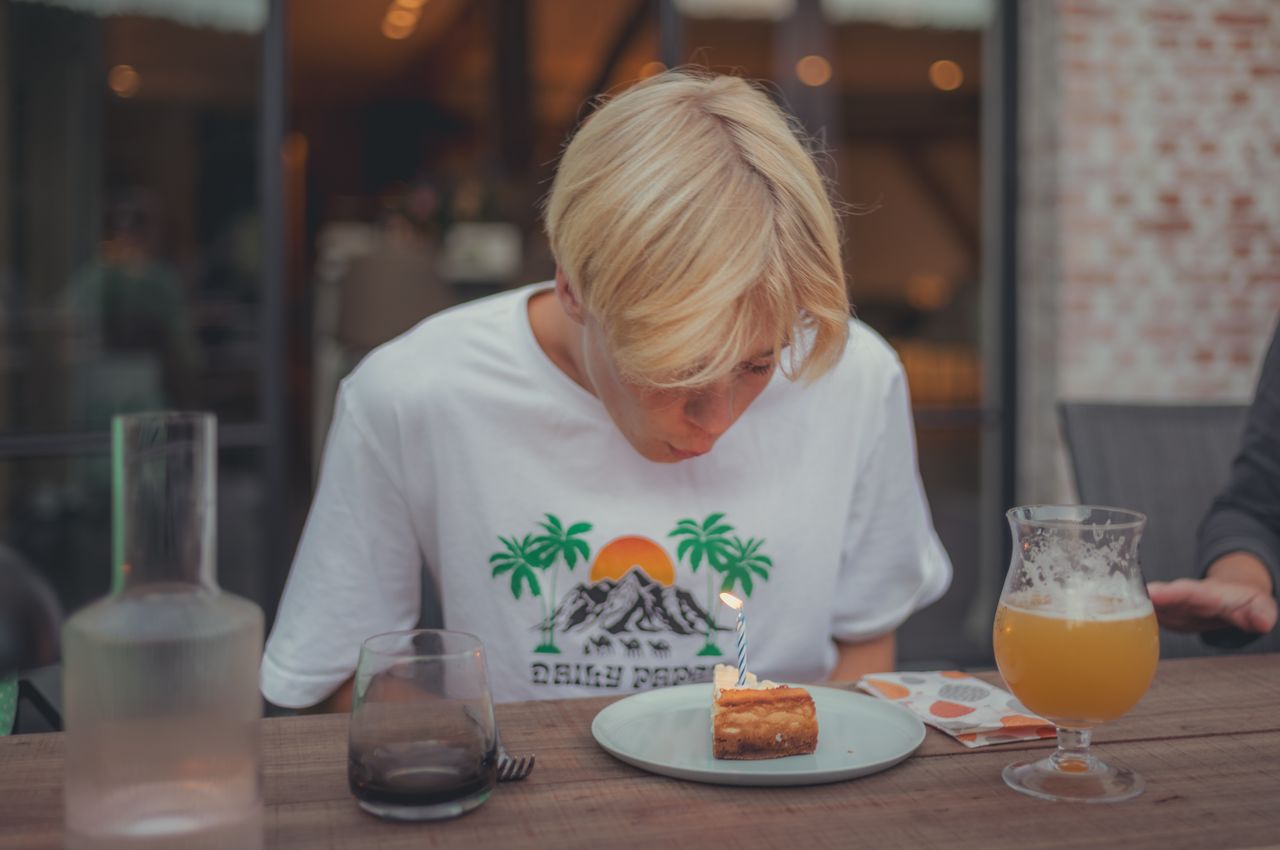 A person leans over to blow out a candle on top of a slice of cheesecake.