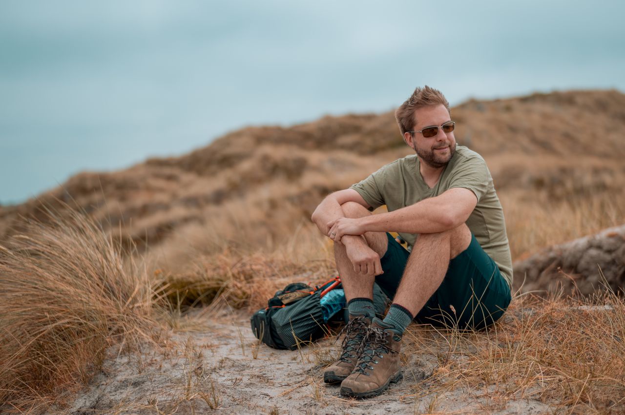 Dries sitting on top of a dune with his backpack next to him.