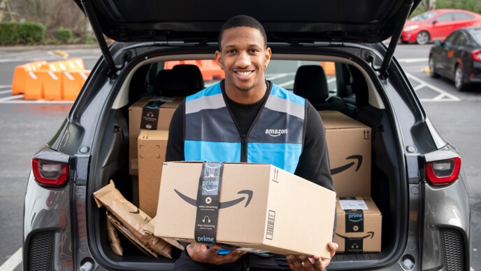 A photo of Quarterback Michael Penix Jr., sitting on the edge of a trunk of a car, holding and Amazon delivery box.