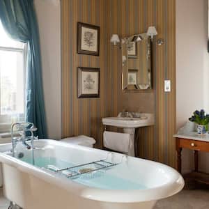 A free standing bathtub and stripped wallpaper in a cozy bathroom