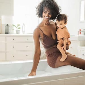 Woman holding child is filling up the bathtub