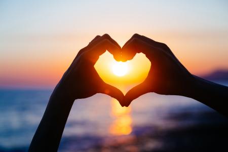 Hands forming a heart shape with sunset silhouette.