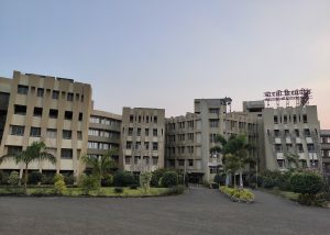 The entrance to Bharati Vidyapeeth College of Engineering in Kolhapur, a large 5-story brown building with palm trees and grass.