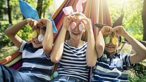 Three kids, two boys and a girl, lying on hammock on sunny spring day. They are playing with Easter eggs.