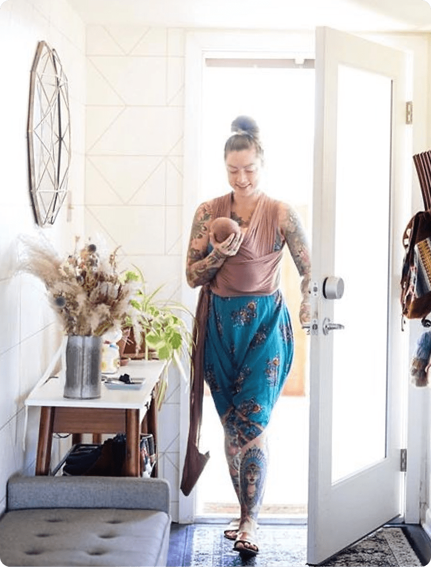 Woman holding a baby using her August smart lock to unlock the front door