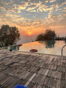 Sunset on a infinity pool of bangladesh. Sairu Hill Resort. Brick patio in the immediate foreground, then the pool, then a long view with the sun setting in the far distance.
