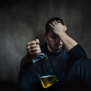 man holding bottle of alcohol with his hand on head and a distressed look.