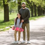 Smilende far og datter holder skateboard i parken