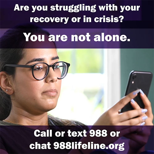 Image of a young woman of color, wearing glasses, looking at her phone. A dark top banner with white text says, “Are you struggling with your recovery or in crisis?” Below a transparent purple overlay with white text says you are not alone. Get support today. Bottom transparent purple banner with white text says call or text 988 or chat 988lifeline.org.