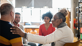 woman putting hand on mans shoulder in group therapy