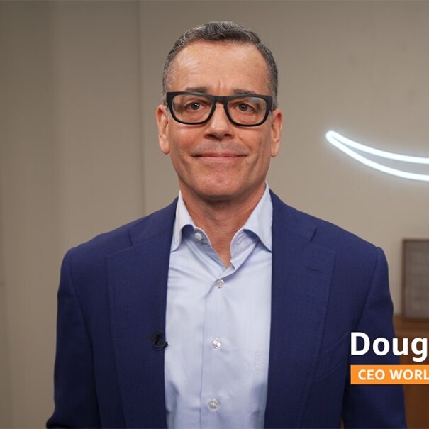 Doug Herrington wears a navy suit and stands in front of a lit up Amazon smile logo hanging on the wall.