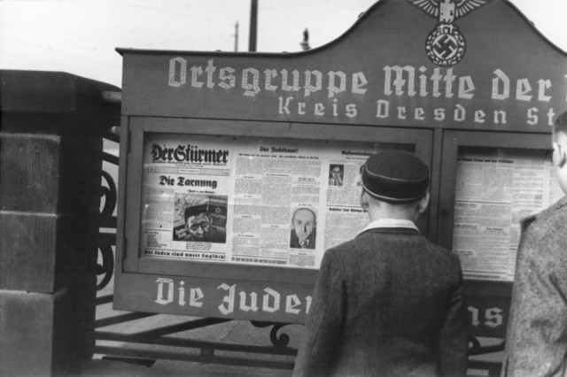 German boys read an issue of Der Stuermer newspaper posted in a display box at the entrance to a Nazi party headquarters in the Dresden region.