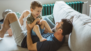 Little boy and his father laughing and playing on the sofa.