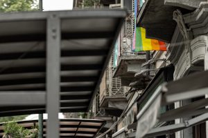 A pride flag hanging on a balcony on a city street.