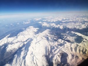 Aerial view of the Pyrenees mountain range with snow-covered peaks under a clear blue sky.