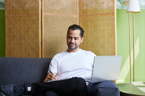 Alberto Villarubia, a UX Design Google Career Certificate graduate, sits on a blue couch while working on his laptop