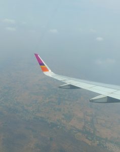 Thai Smile Airways colors on an airplane's wings flying in the sky. The land and the sky are visible in the background.