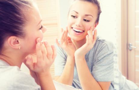 Young woman looking in mirror and smiling.