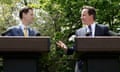 Nick Clegg and David Cameron, both in suits and ties, stand at podiums with microphones in the garden of 10 Downing Street and look at each other, Cameron gesturing with his right hand