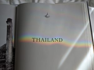 Book opened, "Thailand" on a white page with a rainbow shining over it.