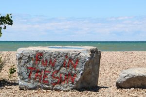 A giant rectangular stone on a stony beach on Lake Ontario. "Fun in the sun" is graffiti'd on it.