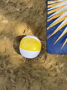 A beach ball and a dark blue blanket on a beach, seen from above.