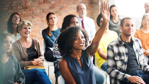 A parent raising her hand in a room full of people.