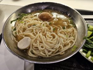 A steaming bowl of Taiwanese noodle soup with a halved tea egg and fish ball.