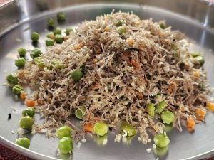 A plate of rice noodles (Vermicelli) topped with green peas and chopped carrots.