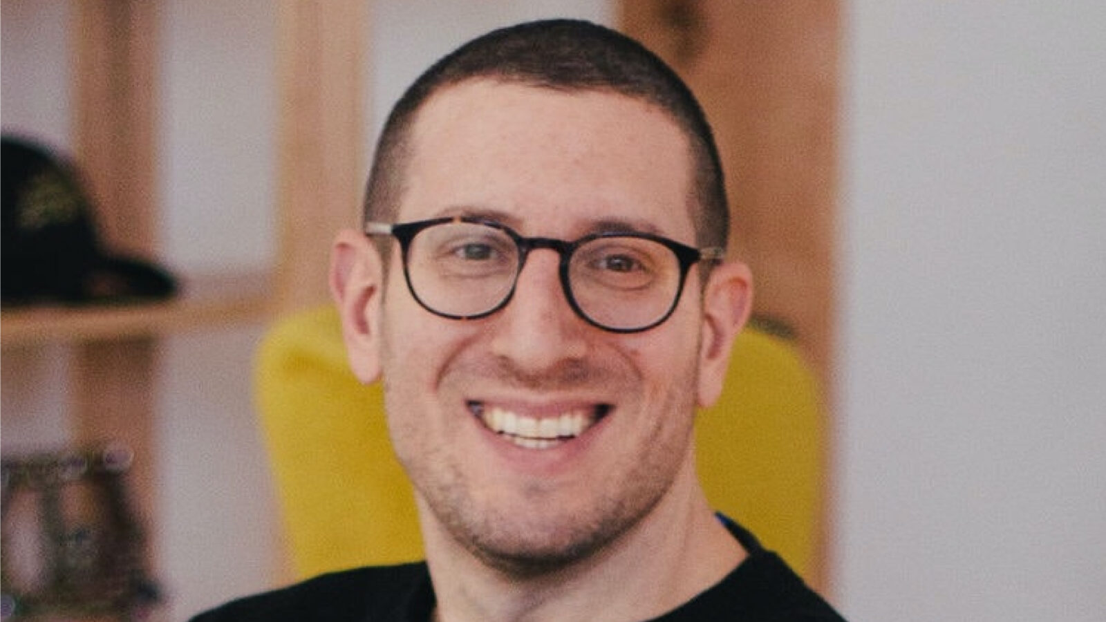 A headshot of a man with glasses smiling.