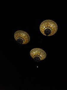 Three intricately patterned and illuminated dome-shaped lamps hang from a dark ceiling, casting a soft yellow glow.