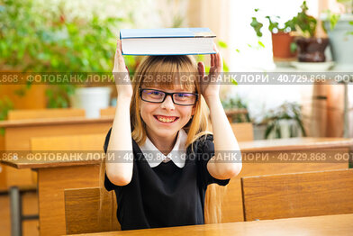 Back to school and happy time. Cute industrious child is sitting at a desk indoors. Kid is learning in classroom. Girl reading the book.